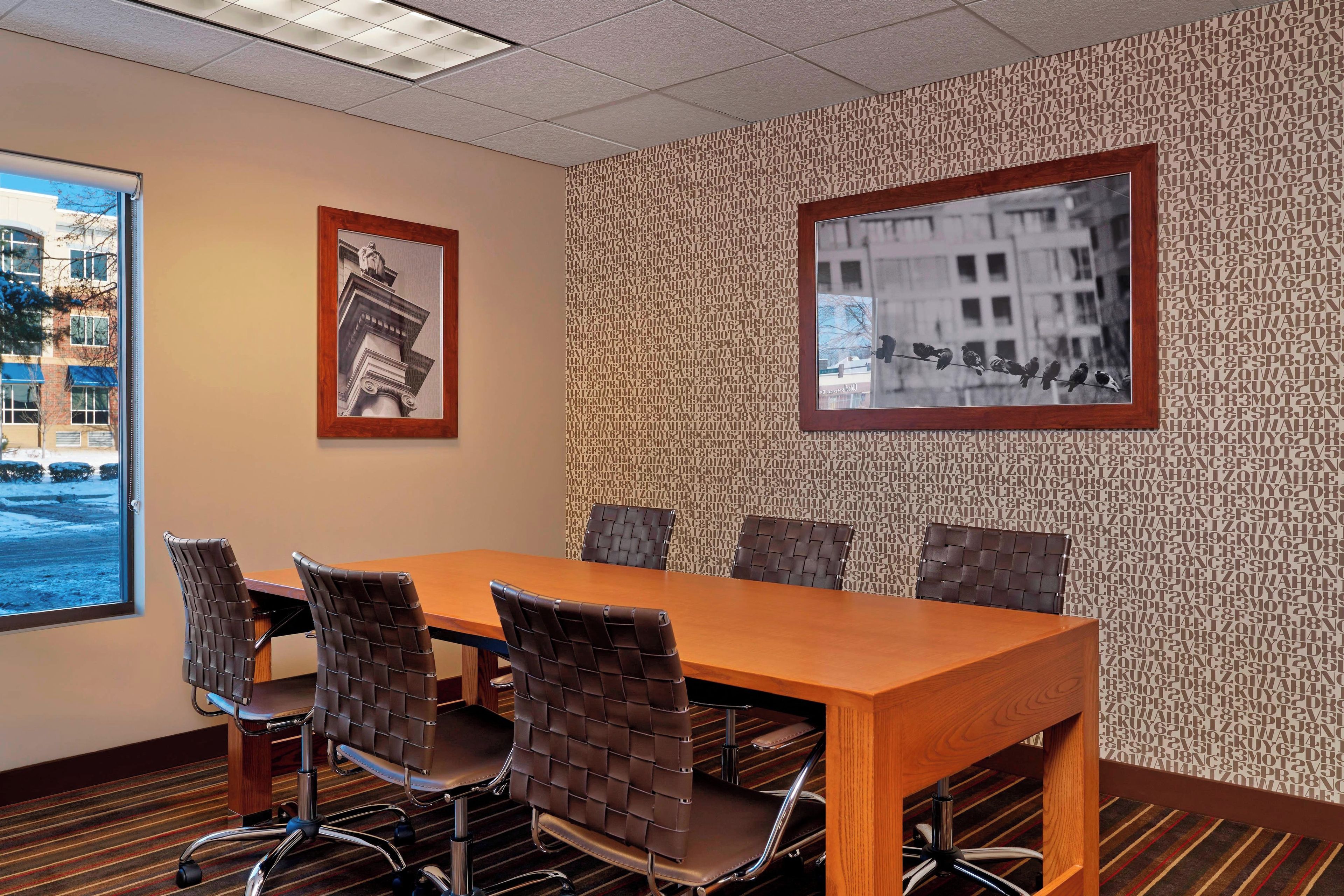 A conference room with a wooden table, four chairs, and two framed pictures on the wall.