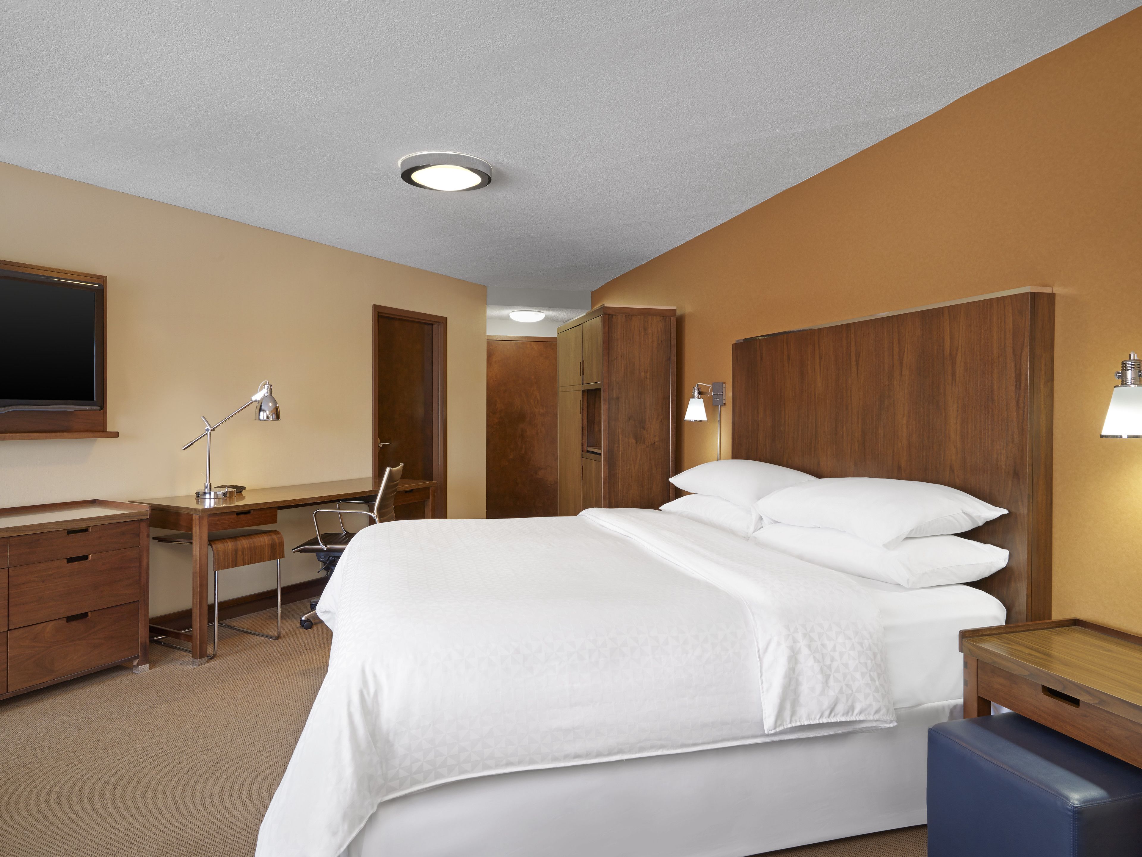 A hotel room with a bed, desk, chair, wardrobe, and a flat-screen TV.