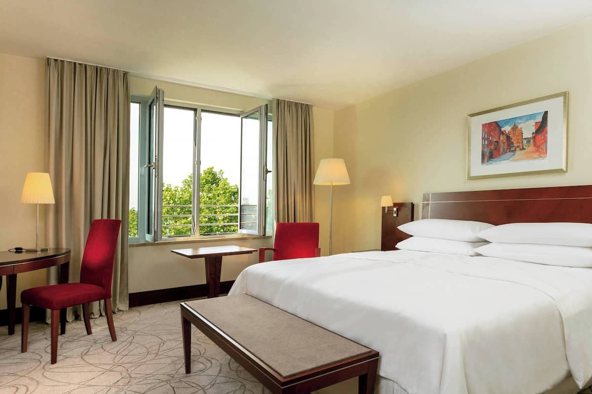 A hotel room with a large bed, two chairs, a small table, and a bench.
