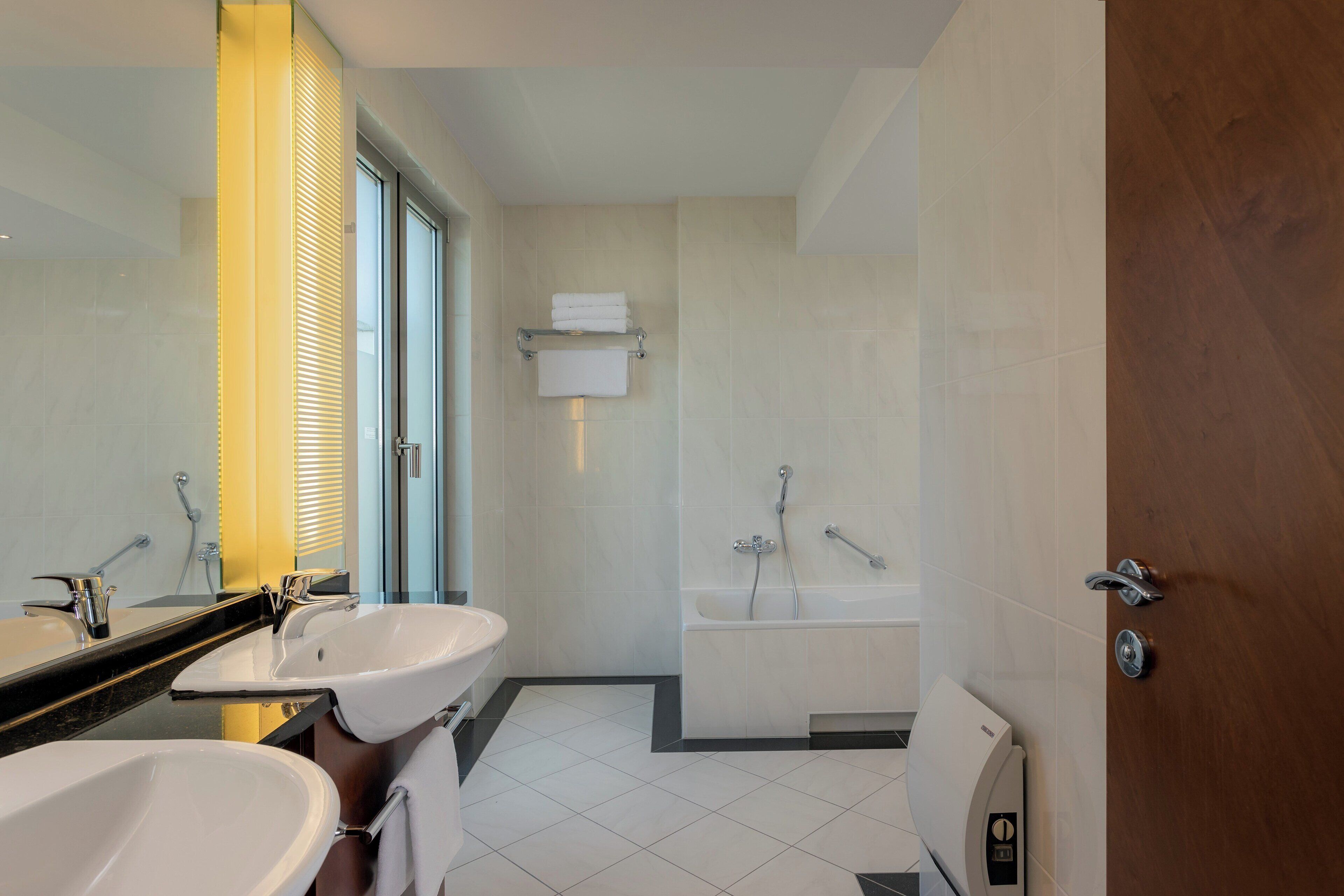 Un baño moderno con dos lavamanos, un espejo grande, una bañera y un perchero para toallas.