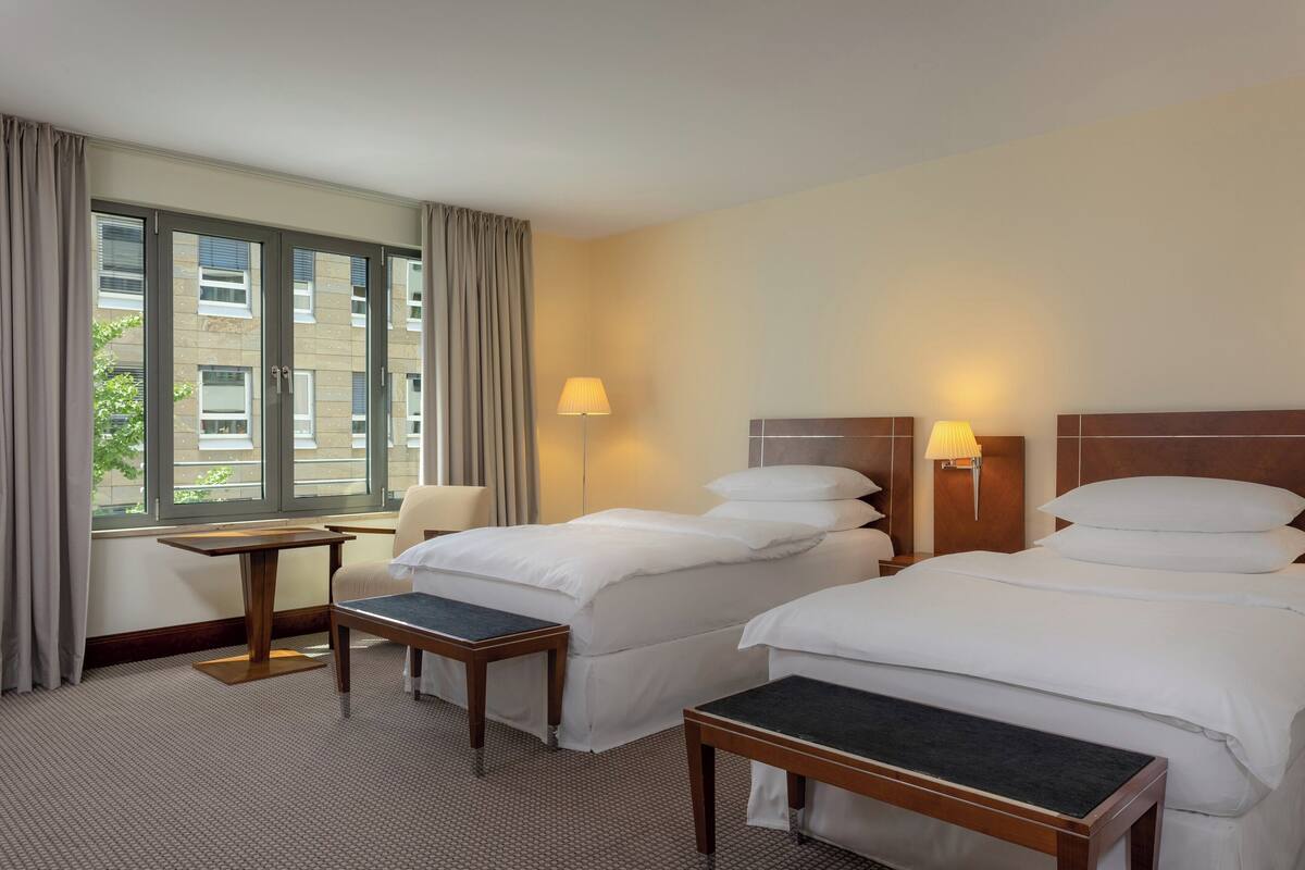 A hotel room with two beds, a desk, a chair, and a window with curtains.