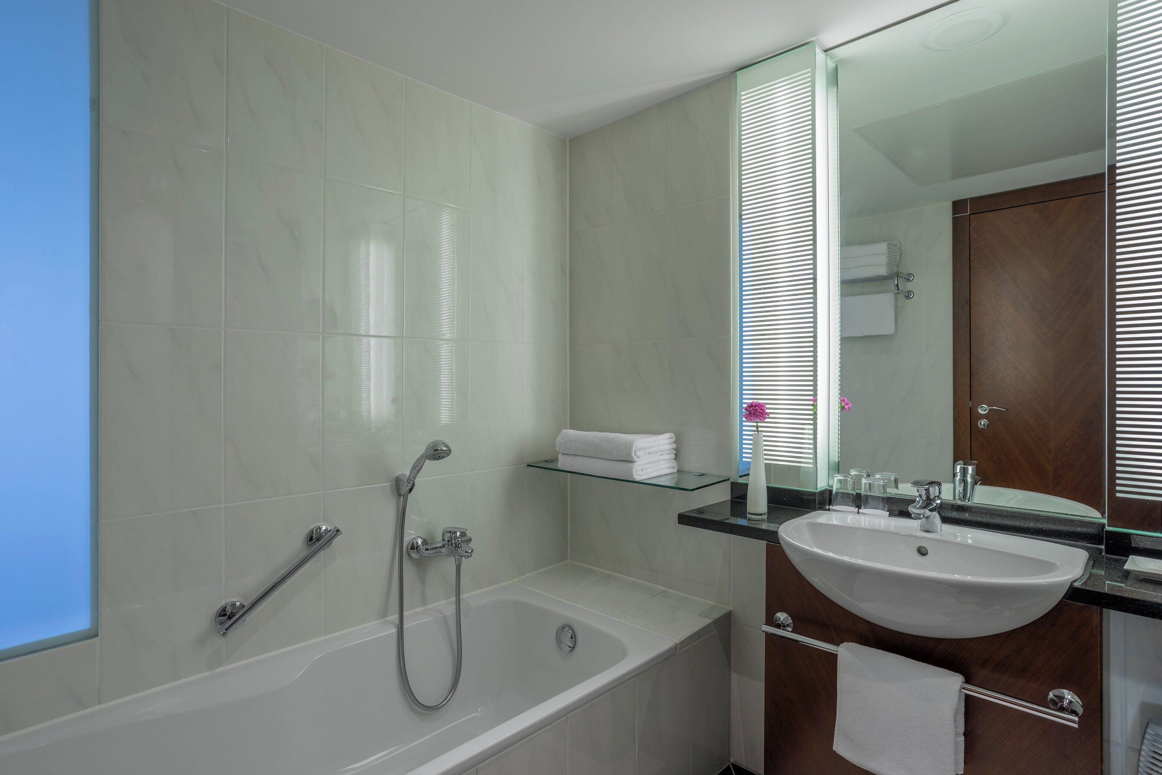 Un baño moderno con una bañera blanca, un estante de vidrio con toallas y un espejo grande sobre el lavabo.