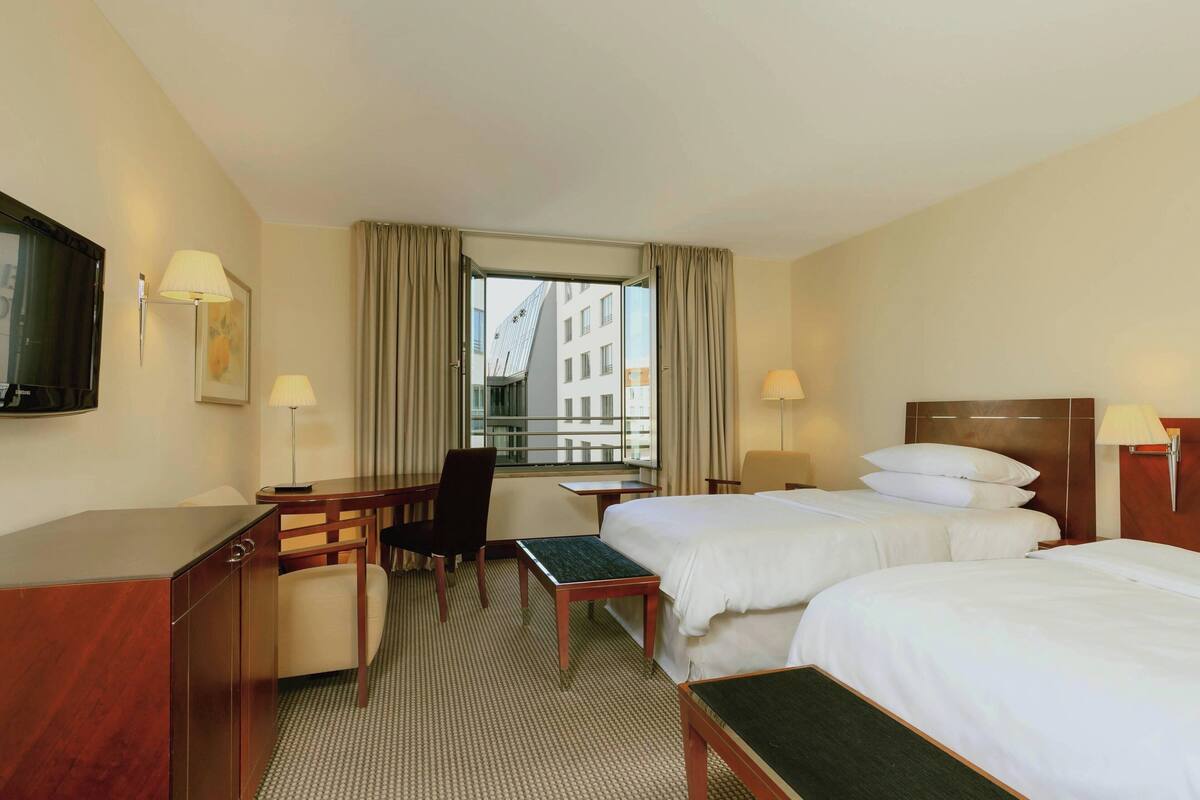 A hotel room with two beds, a desk, a chair, a TV, and a window with curtains.