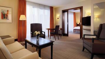 Ein Hotelzimmer mit einer Sitzecke, einem Esstisch, einem Fernseher und einem Bett.