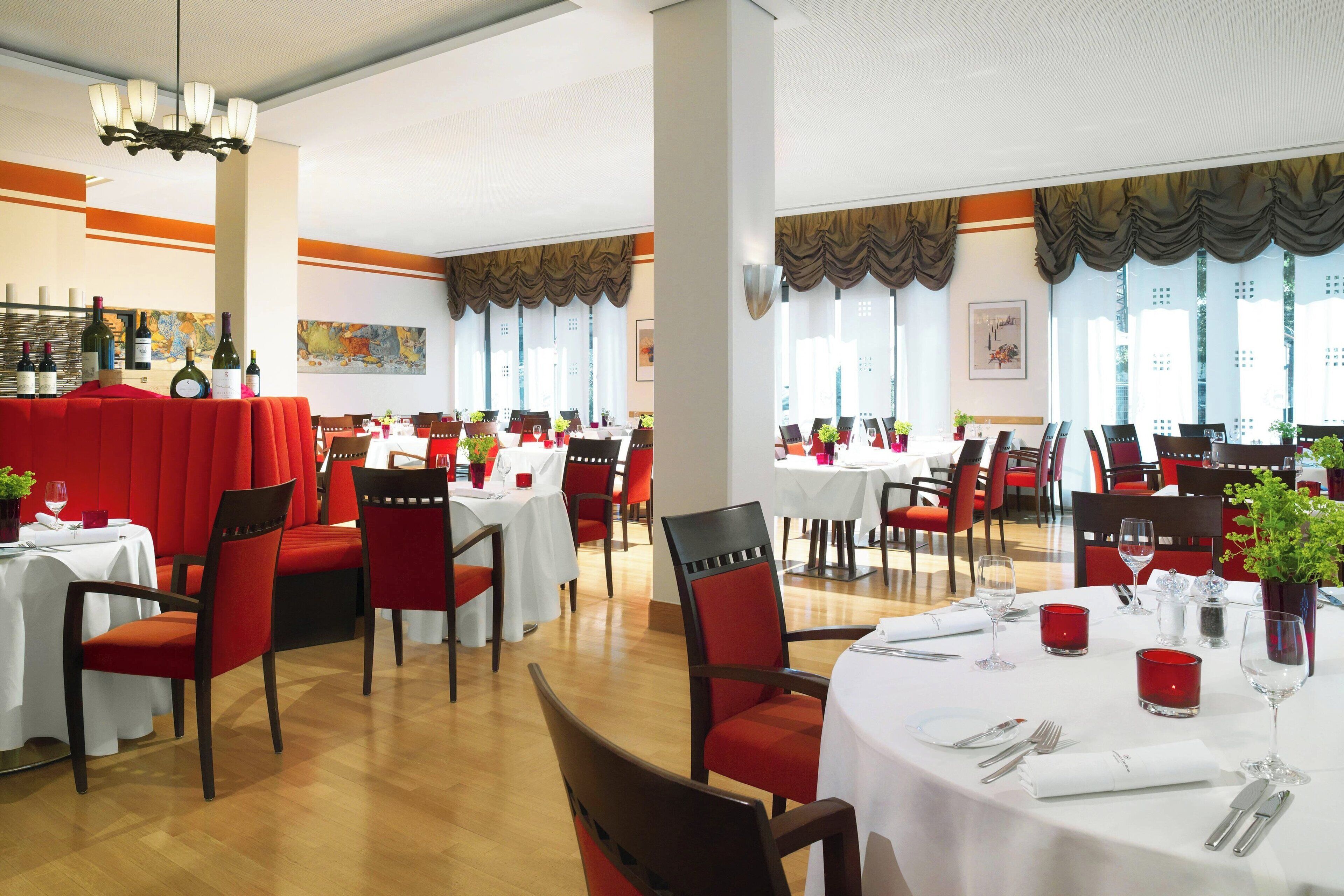 A restaurant with multiple tables and chairs, each set with white tablecloths and red chairs.