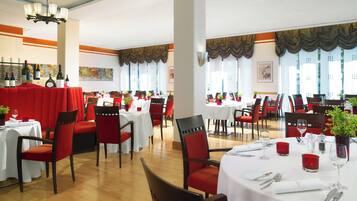 A restaurant with multiple tables and chairs, each set with white tablecloths and red chairs.