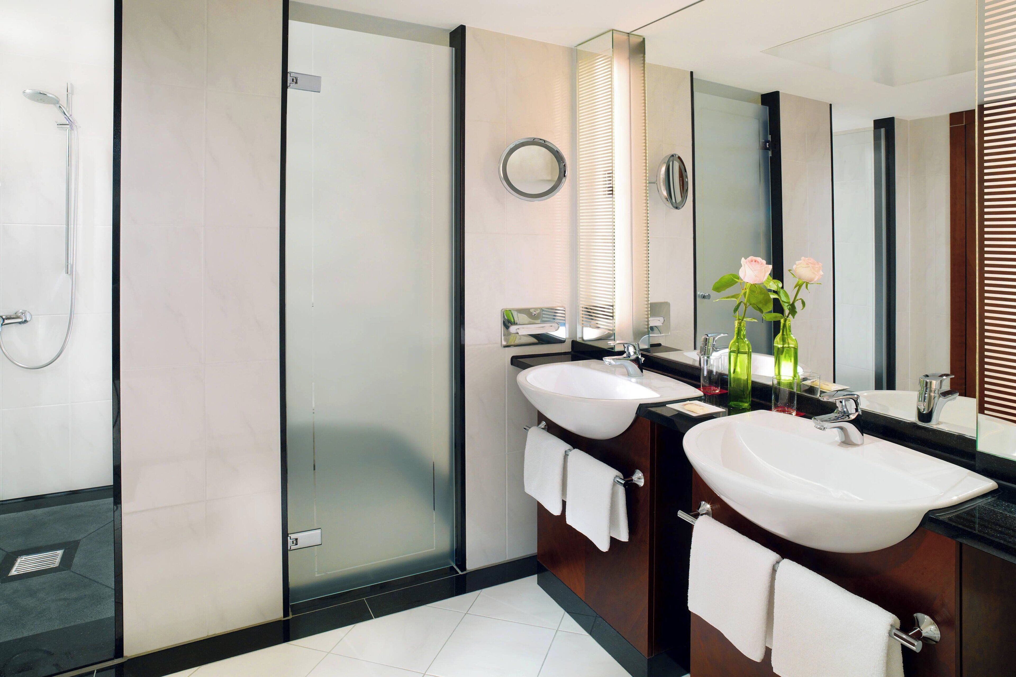 Un baño moderno con dos lavamanos, cabina de ducha de vidrio y un espejo grande.