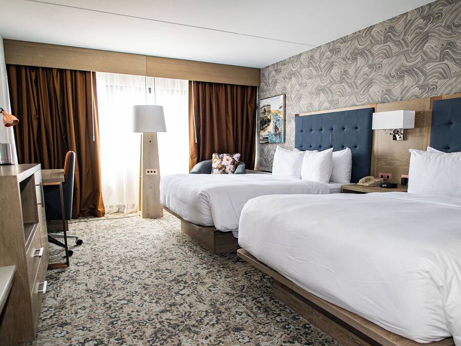 Hotelkamer met twee bedden, een bureau, een stoel, een lamp en een kamerbreed tapijt met een patroon.