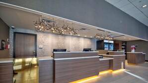 Zona de recepción de un hotel con diseño moderno, que incluye un mostrador de recepción, un espejo grande y una araña.