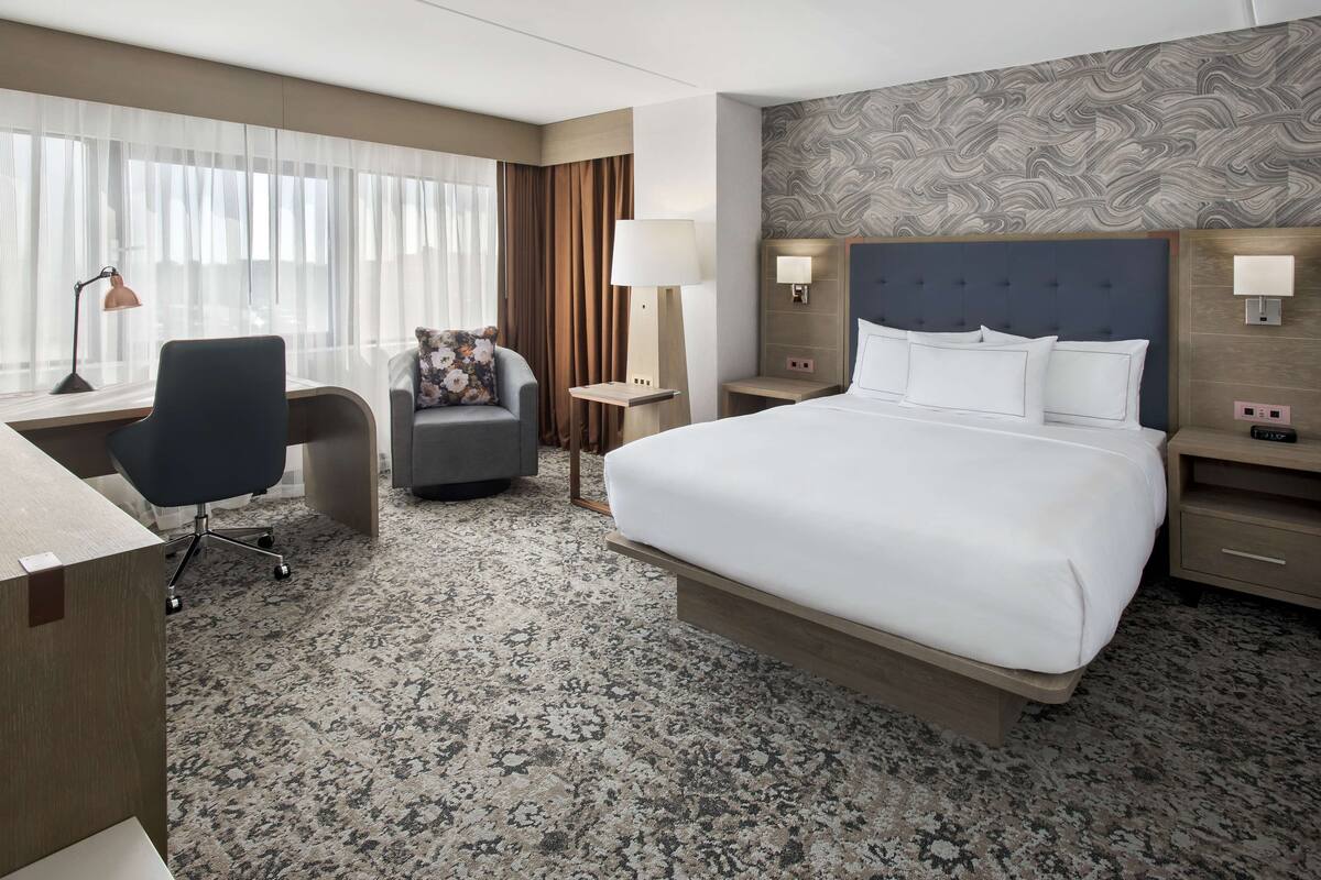 A hotel room with a large bed, a desk, a chair, and a small table.