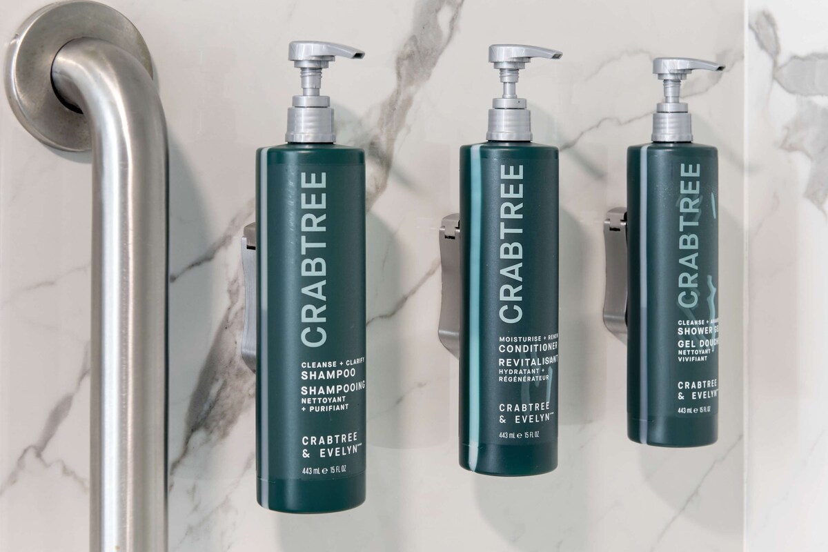 Three bottles of Crabtree & Evelyn shampoo and conditioner on a marble wall.