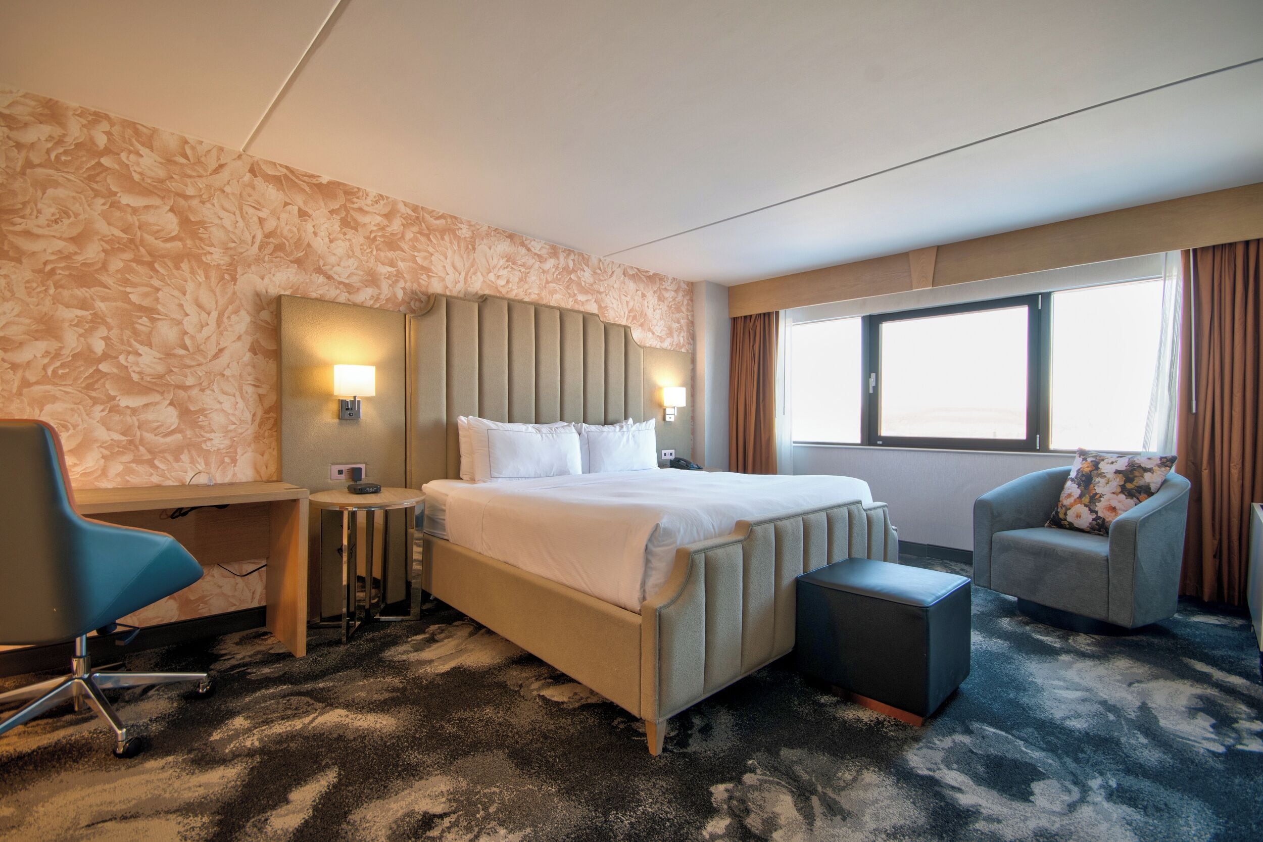 A hotel room with a bed, two bedside tables, a desk, a chair, and a window with curtains.
