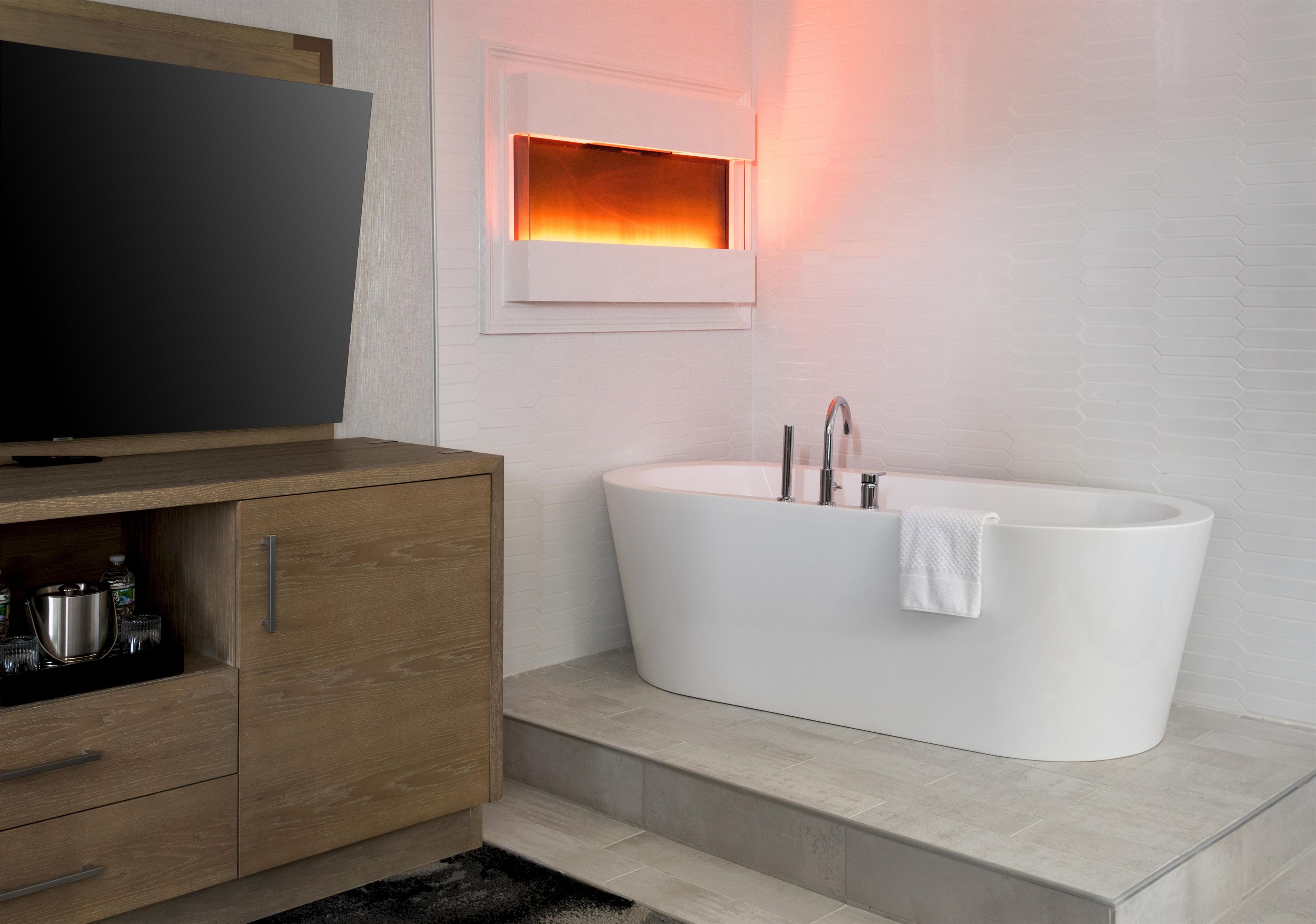 A modern bathroom with a freestanding bathtub, a wooden vanity with a television above it, and a hexagonal light fixture above the bathtub.