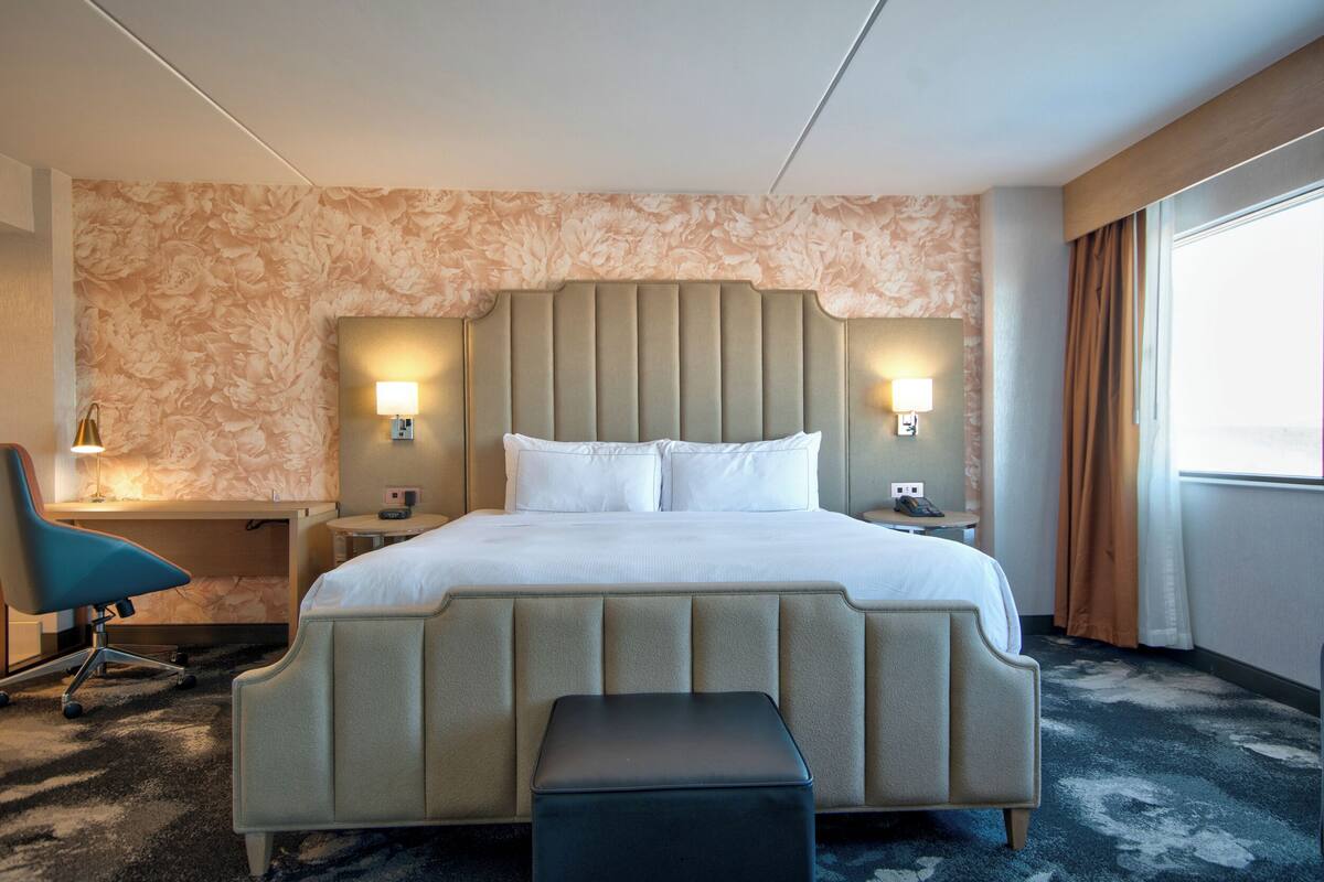 A hotel room with a bed, bedside tables, a chair, and a window.