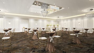 A spacious banquet hall with round tables, chairs, and a high ceiling with chandeliers.