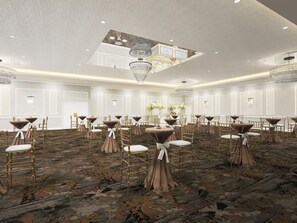 A spacious banquet hall with round tables, chairs, and a high ceiling with chandeliers.