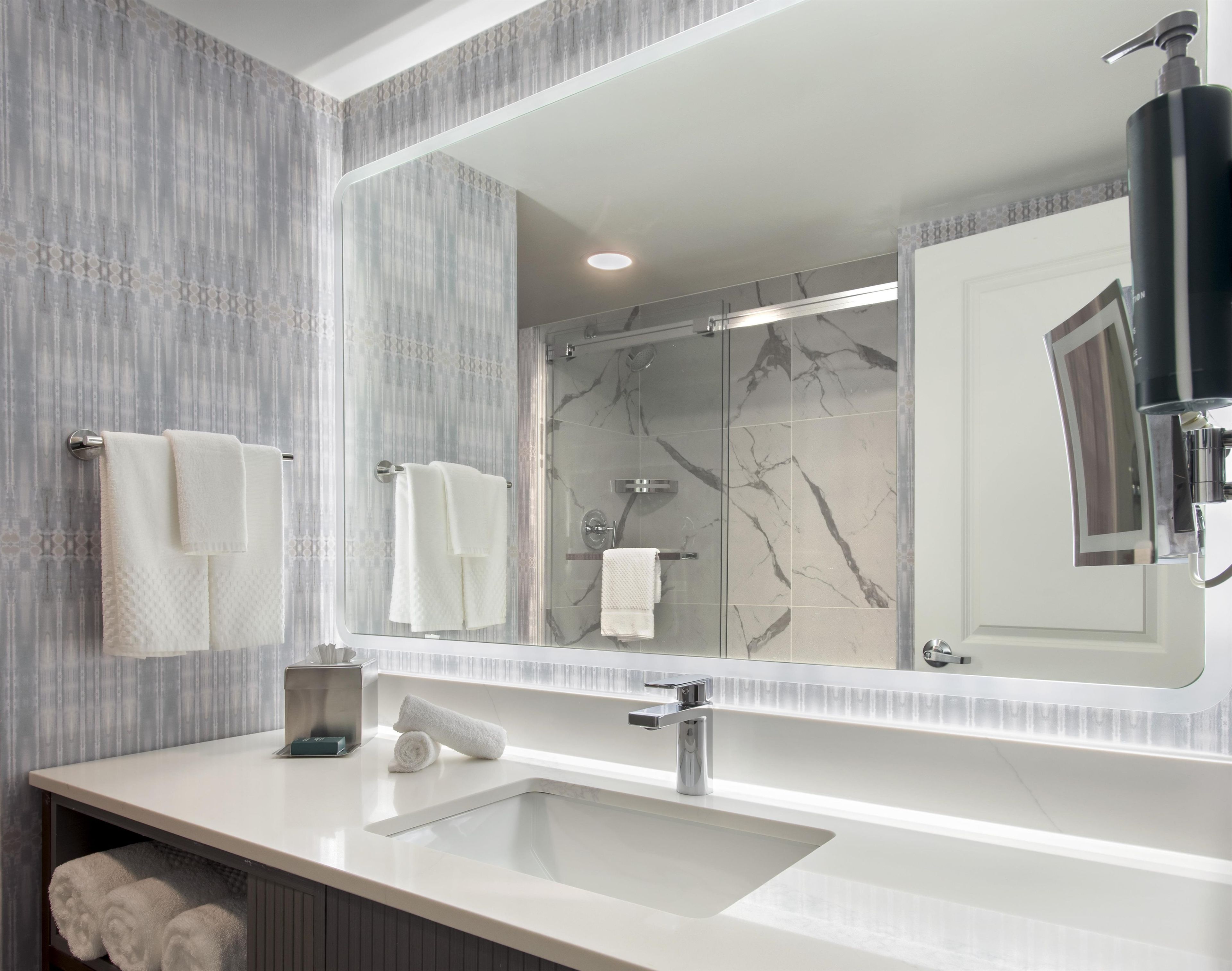 Un baño moderno con un espejo grande, un lavabo y una zona de ducha.