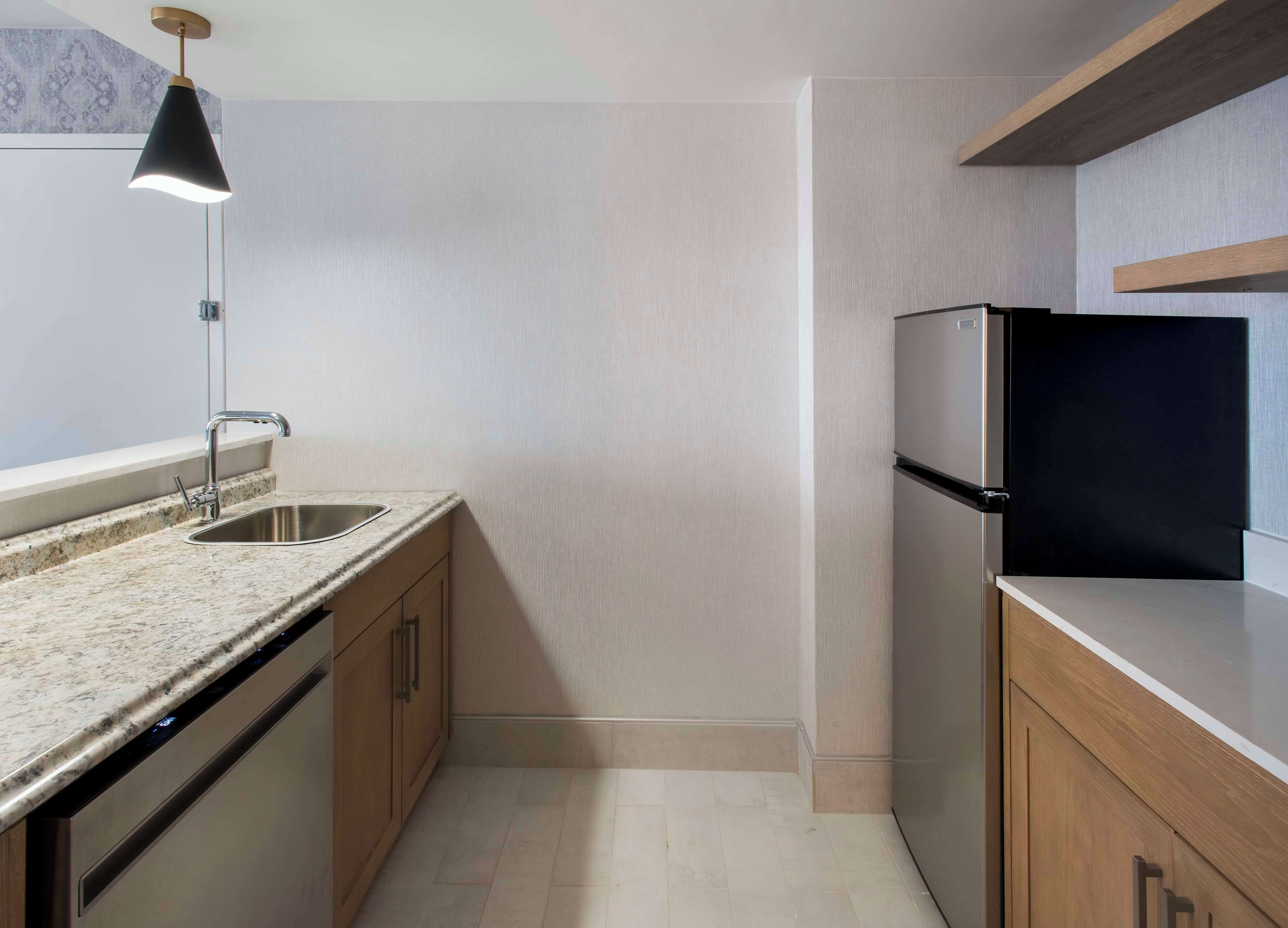 A modern kitchen with a granite countertop, stainless steel sink, and a black refrigerator.
