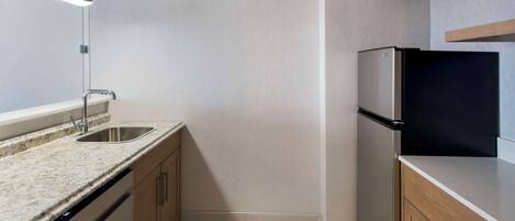 A modern kitchen with a granite countertop, stainless steel sink, and a black refrigerator.