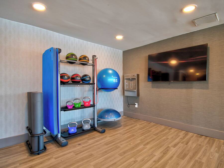 Une salle de remise en forme équipée de matériel d’exercice, dotée d’un téléviseur fixé au mur et d’un plancher en bois.