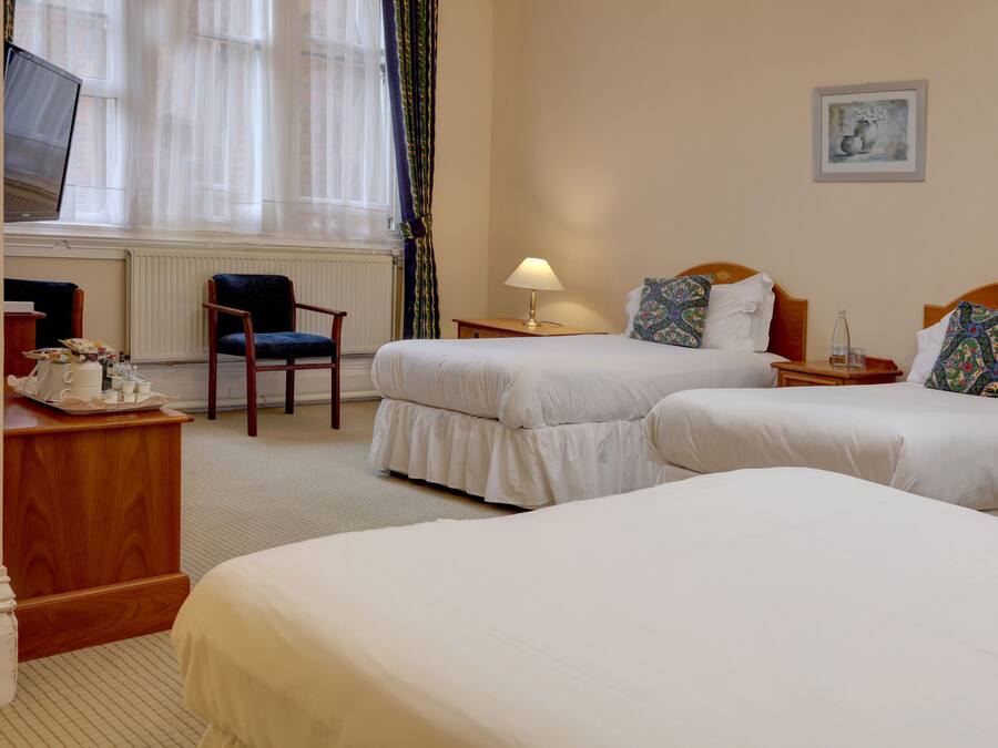 A hotel room with two beds, a desk with a computer, a chair, a lamp, and a painting on the wall.