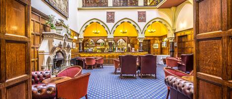 A grand lobby with a high ceiling, ornate wood paneling, and a central bar area.
