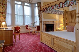A bedroom with a wooden bed, a fireplace, a desk with a chair, and a small table with chairs.