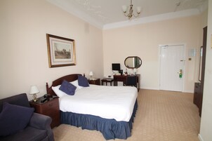 A hotel room with a large bed, a desk with a mirror, a dresser, a chair, and a framed picture on the wall.
