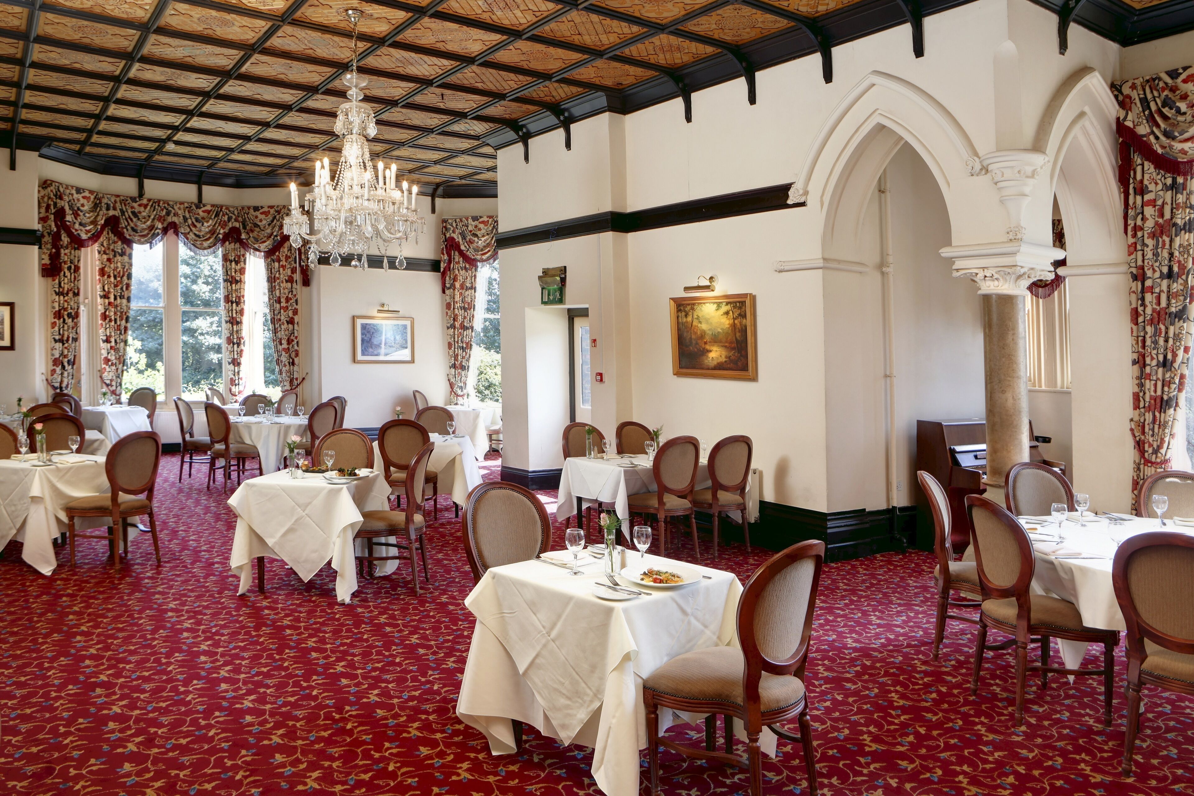 A formal dining room with tables set for service, chandeliers, and classical architecture.
