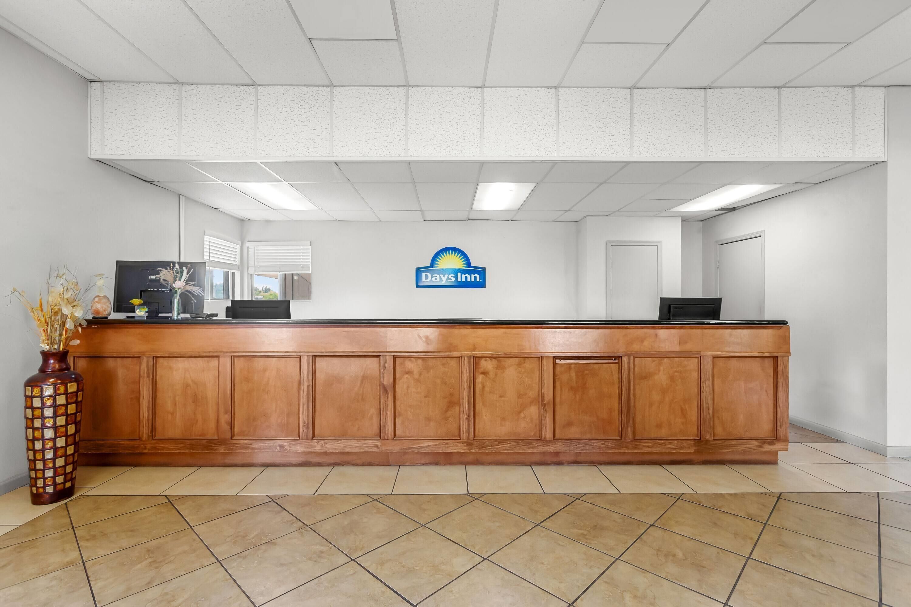 A reception desk with a Days Inn sign, a wooden counter, and a vase with dried flowers.
