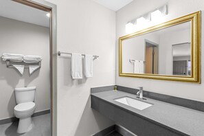 A modern bathroom with a white toilet, a grey sink with a gold-framed mirror, and two towels hanging on a rack. - Days Inn by Wyndham Huntington (Huntington)