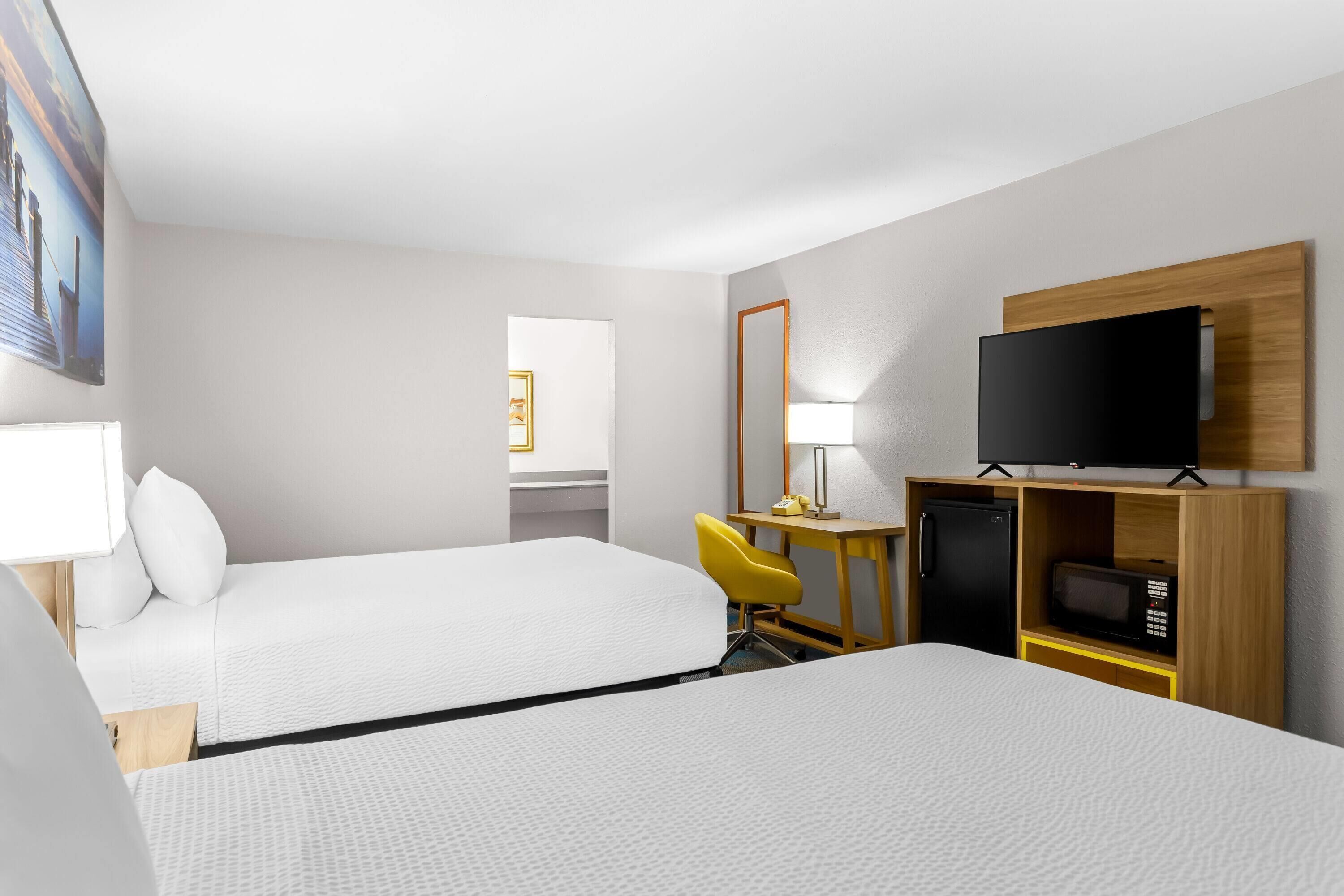 A hotel room with two beds, a desk with a chair, a television, a microwave, and a small refrigerator.