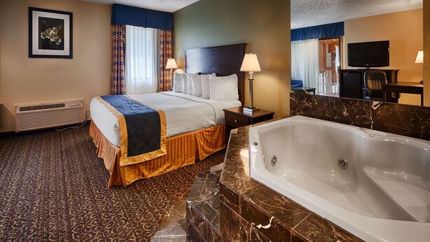 Habitación de hotel con cama, una bañera grande, televisión y escritorio con lámpara.