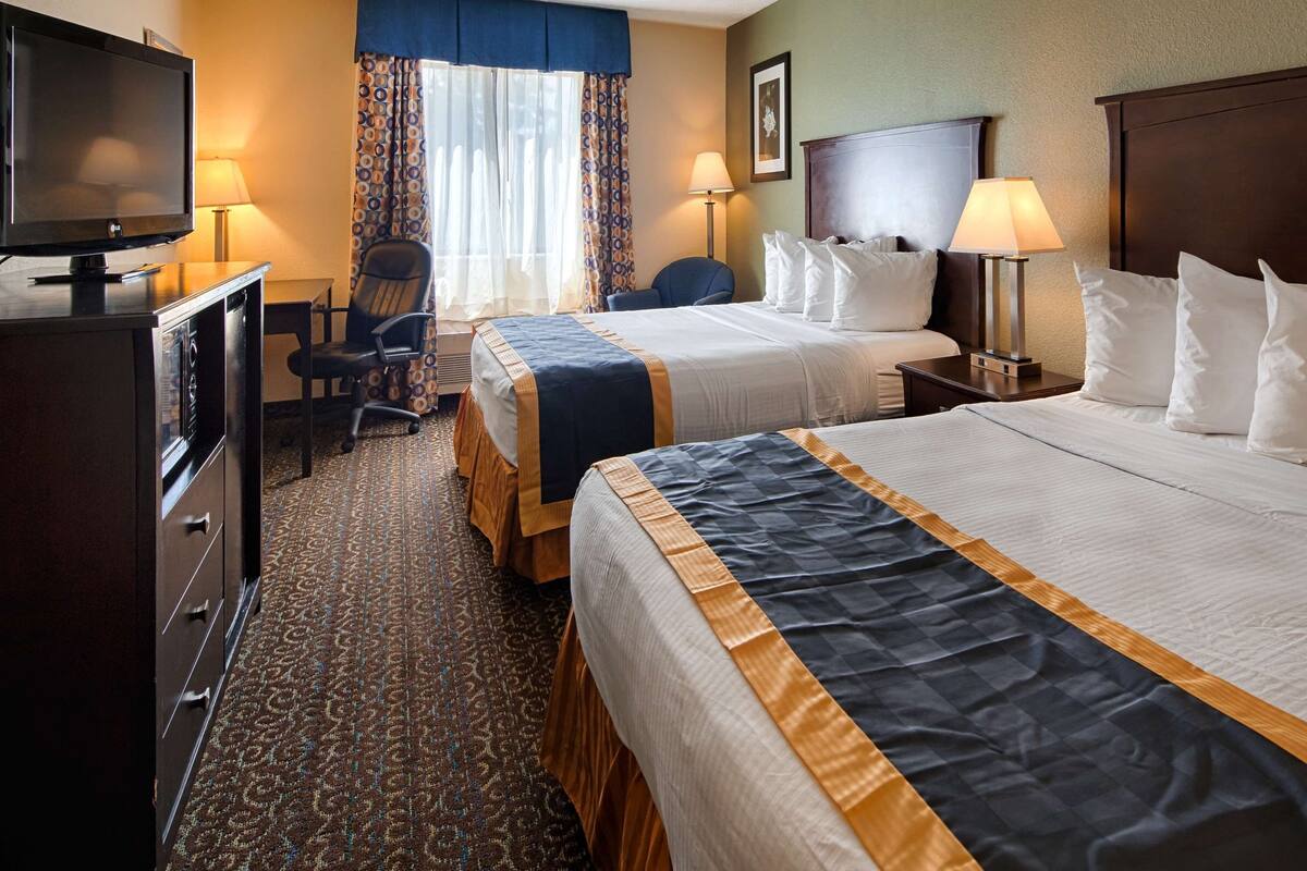 A hotel room with two beds, a desk with a television, a chair, and a desk lamp.