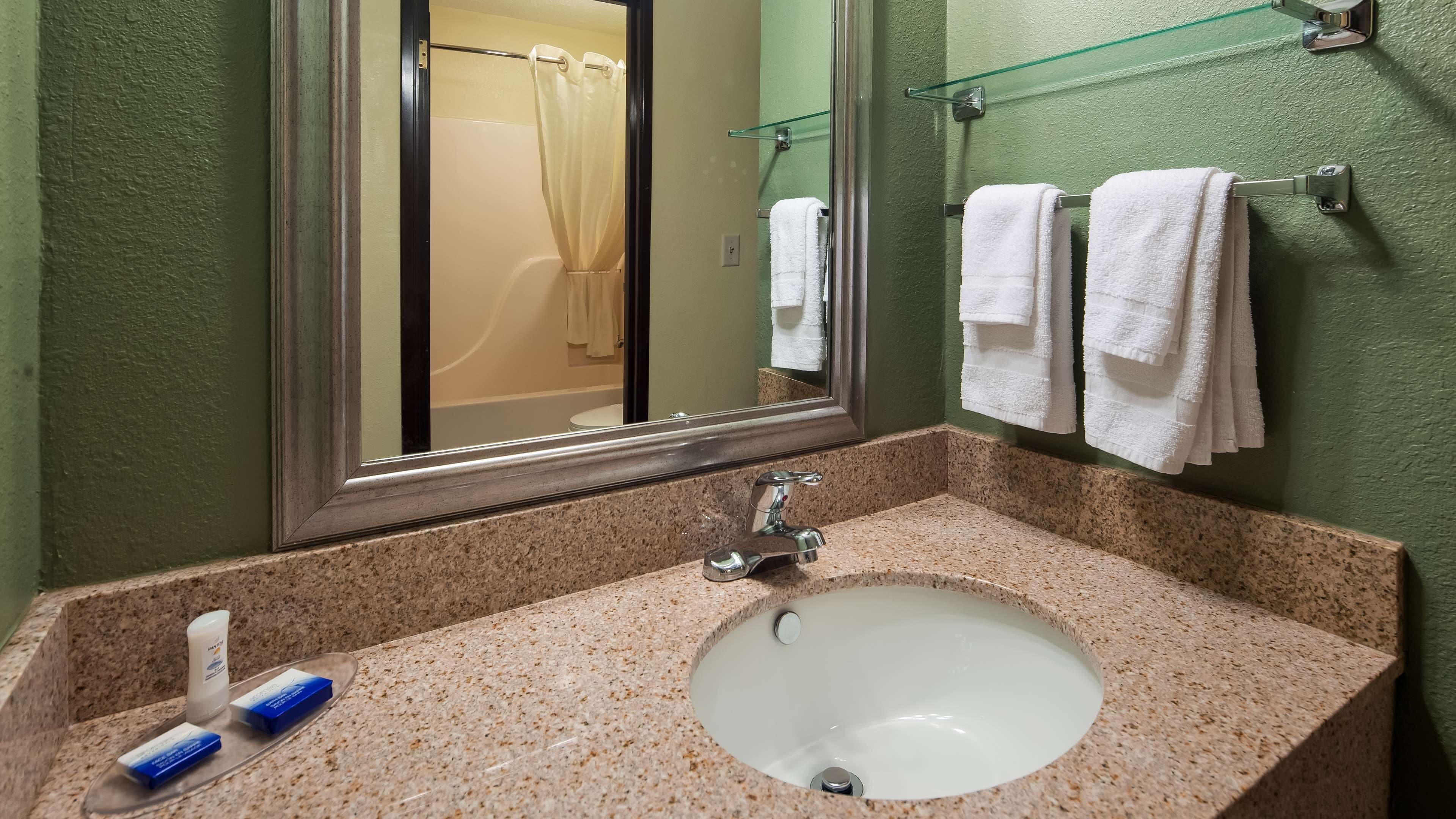 Un bagno con un piano di lavoro in granito, un lavandino bianco e uno specchio. Due asciugamani bianchi sono appesi a un portaservizi.