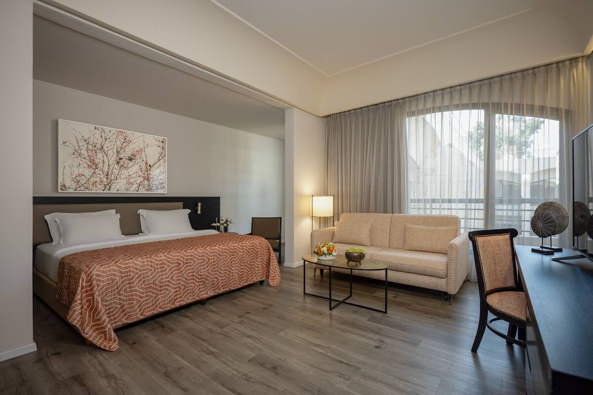 A hotel room with a bed, a sofa, a coffee table, and a chair.