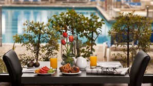 A breakfast table with fruits, pastries, and beverages, overlooking a pool with lounge chairs. - Dan Jerusalem (Jerusalem)