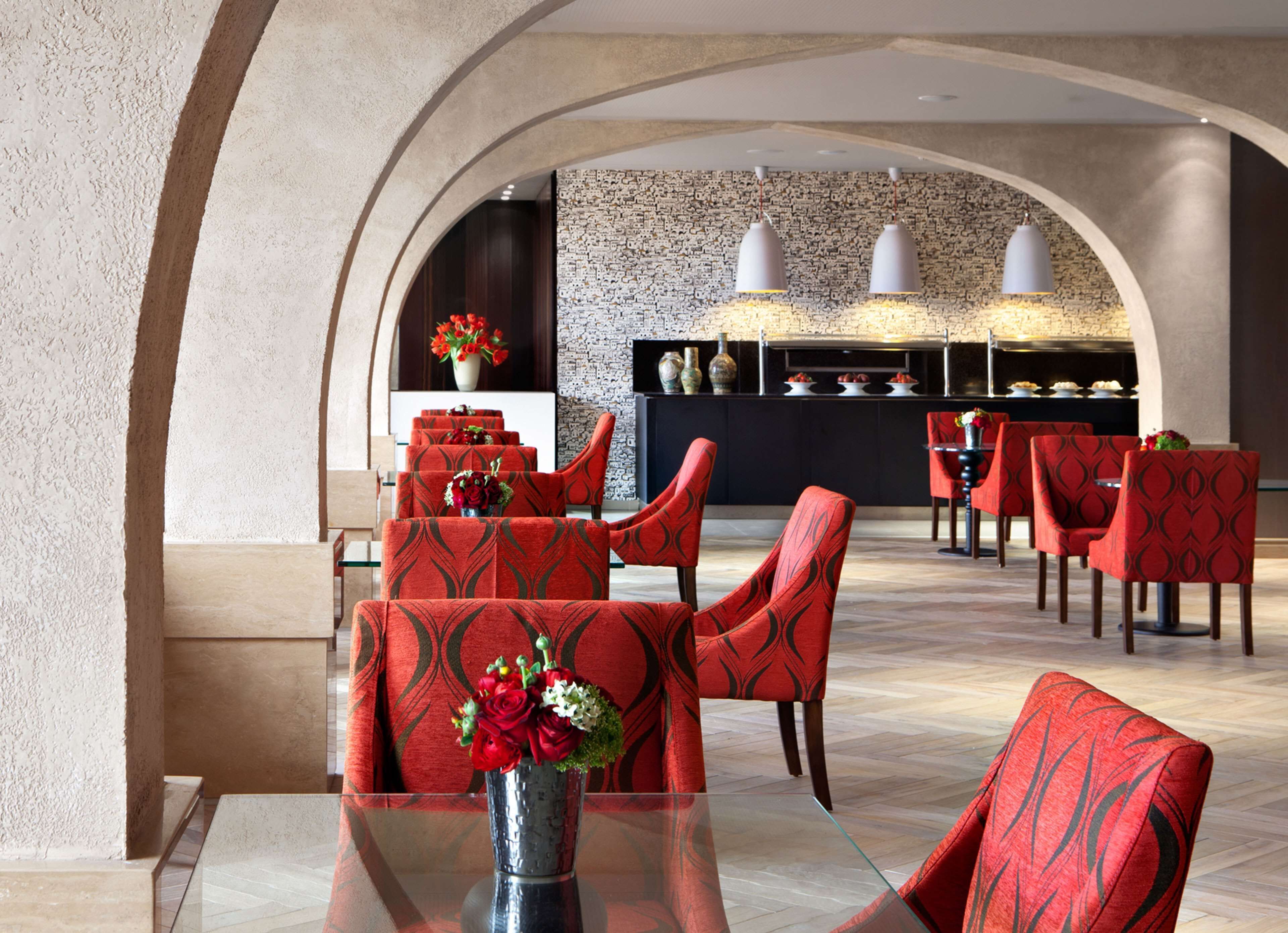 A modern dining area with red patterned chairs, a glass table, and a decorative vase with flowers.