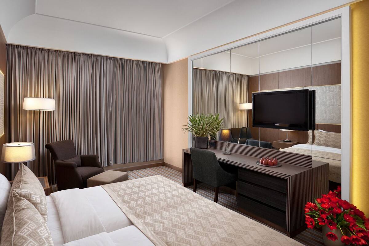 A hotel room with a bed, a desk, a chair, a TV, and a mirror.