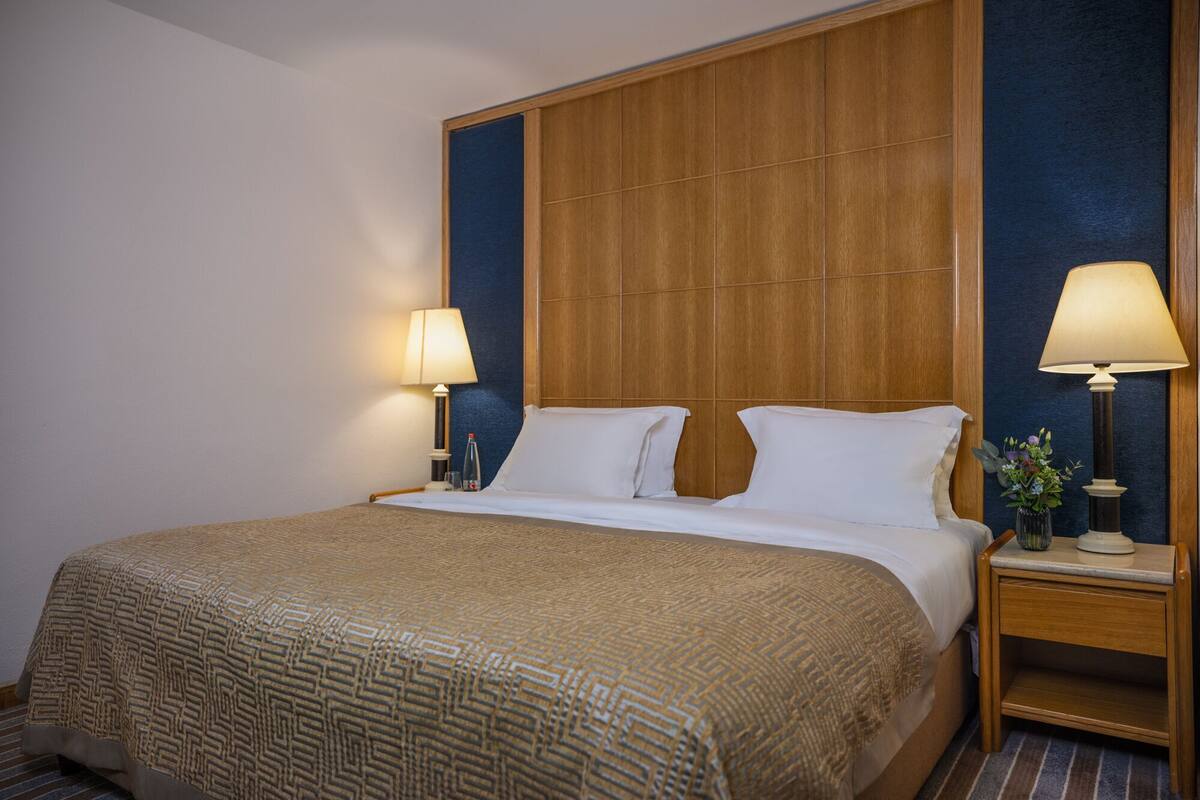 A hotel room with a large bed, two bedside tables with lamps, a wooden headboard, and a blue accent wall.