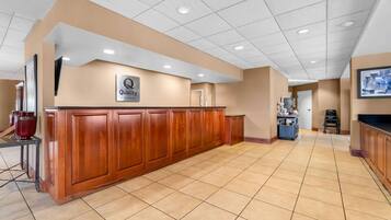 A hotel lobby with a reception desk, a sign reading 'Quality by Choice Hotels,' and a tiled floor.