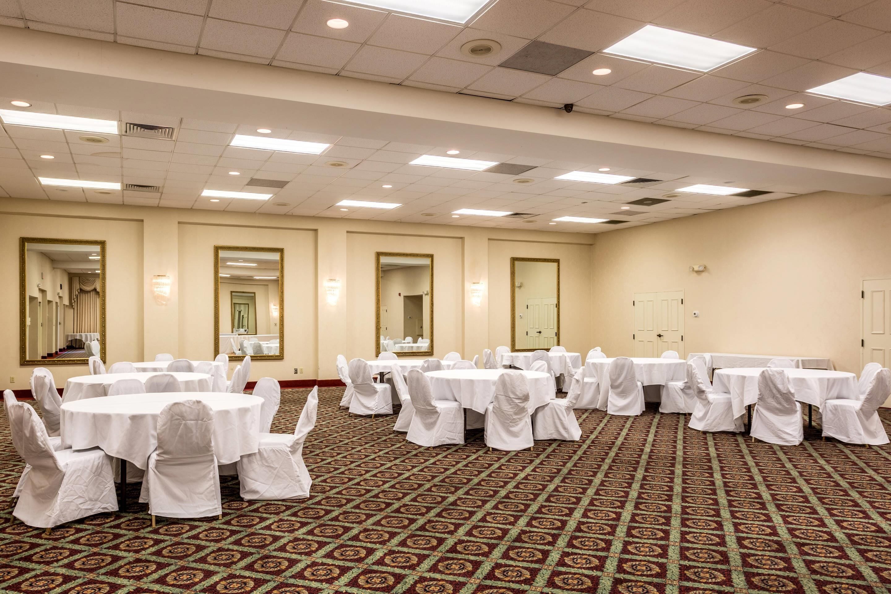 A conference room with multiple round tables and chairs, carpeted floor, and ceiling lights.