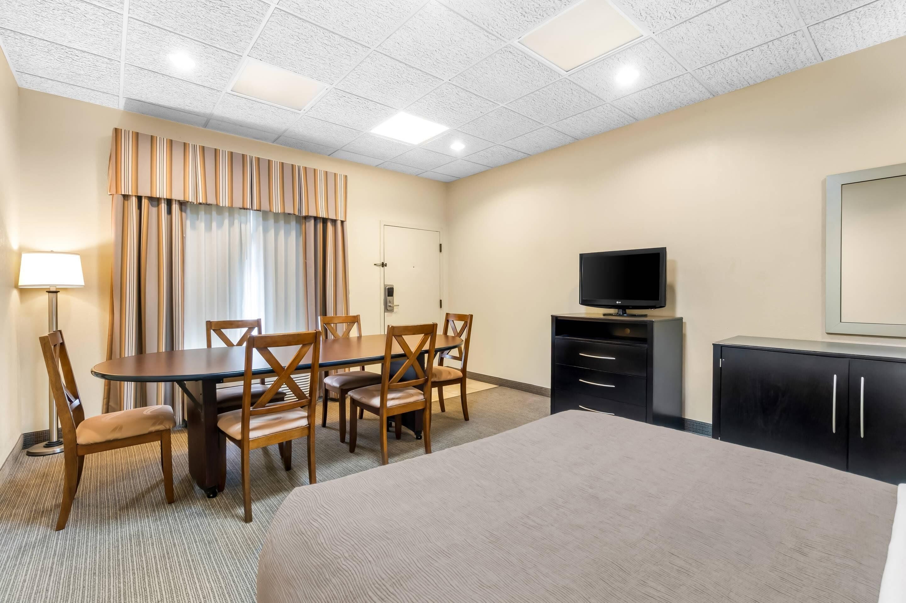 Una habitación de hotel con cama, escritorio con sillas, televisión y armario.