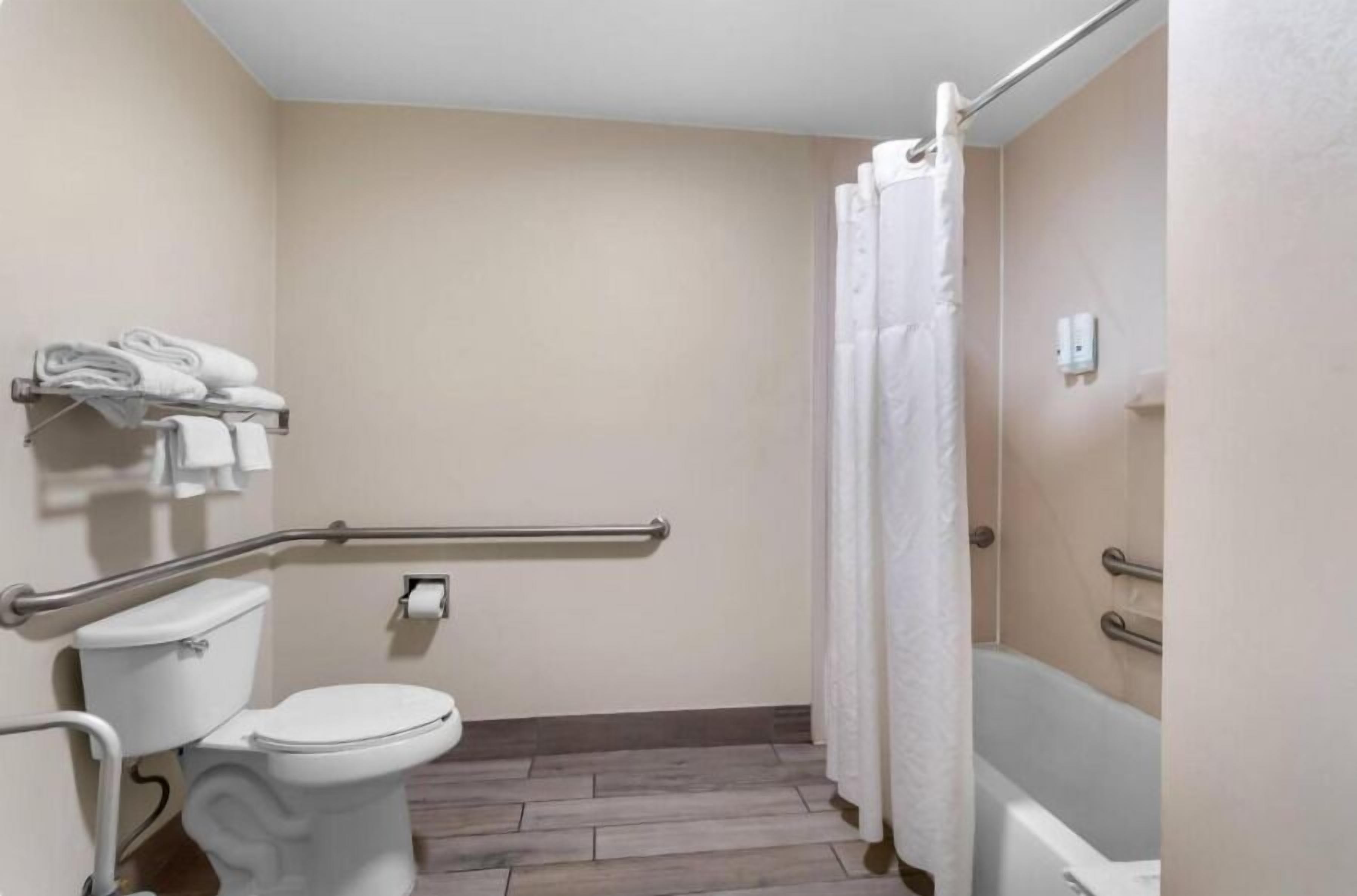 A bathroom with a toilet, a shower with a curtain, a grab bar, and a towel rack with folded towels.