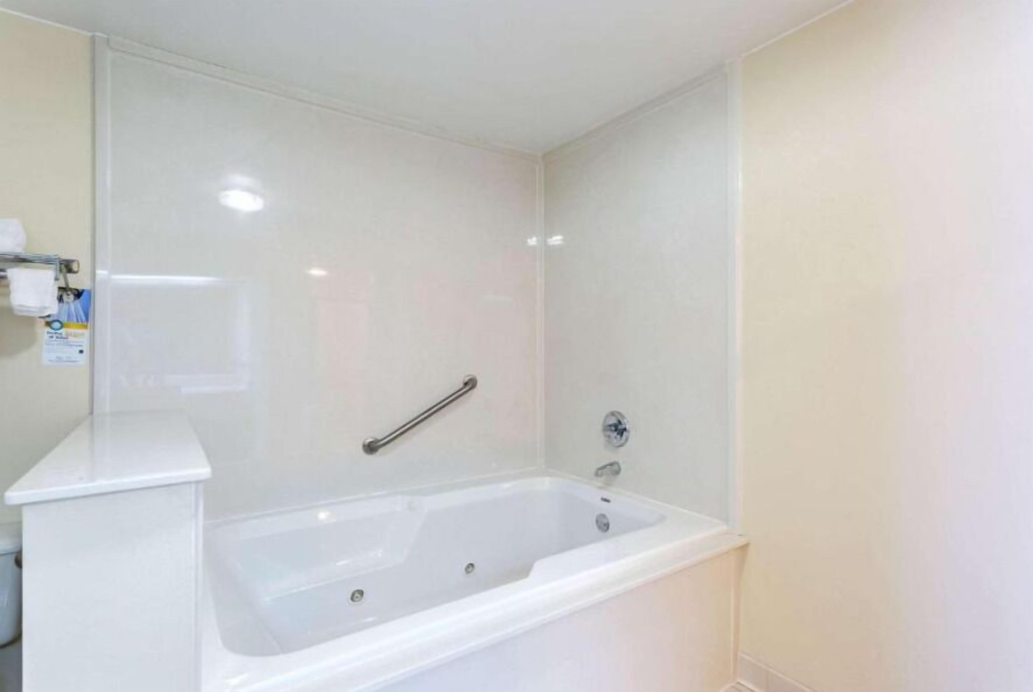 A bathroom with a white bathtub, a handrail, and a white wall.