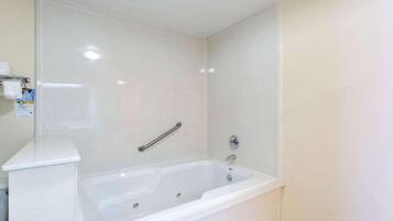 A bathroom with a white bathtub, a handrail, and a white wall.