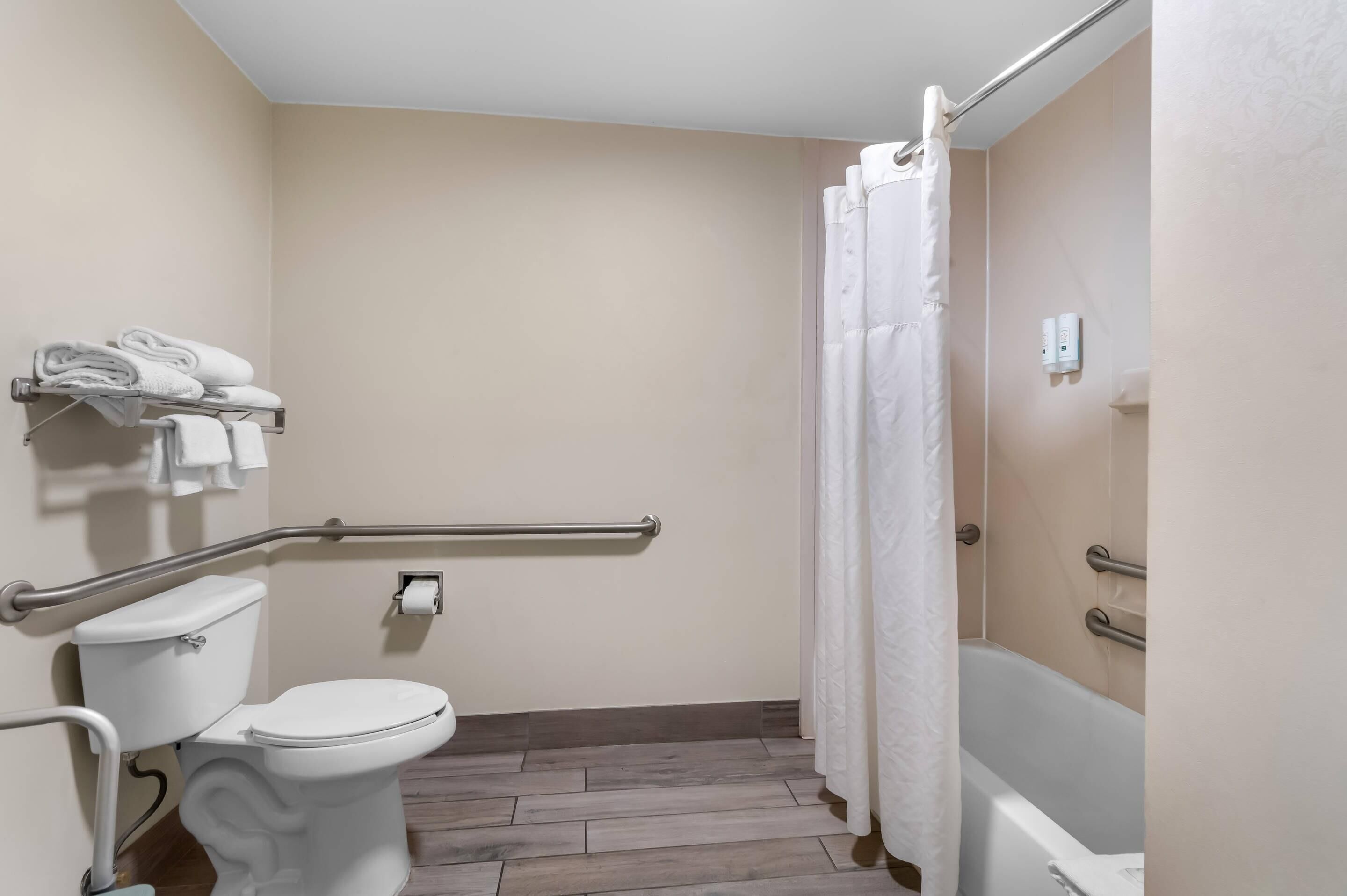 A bathroom with a toilet, a shower with a white curtain, a grab bar, and a towel rack with folded towels.