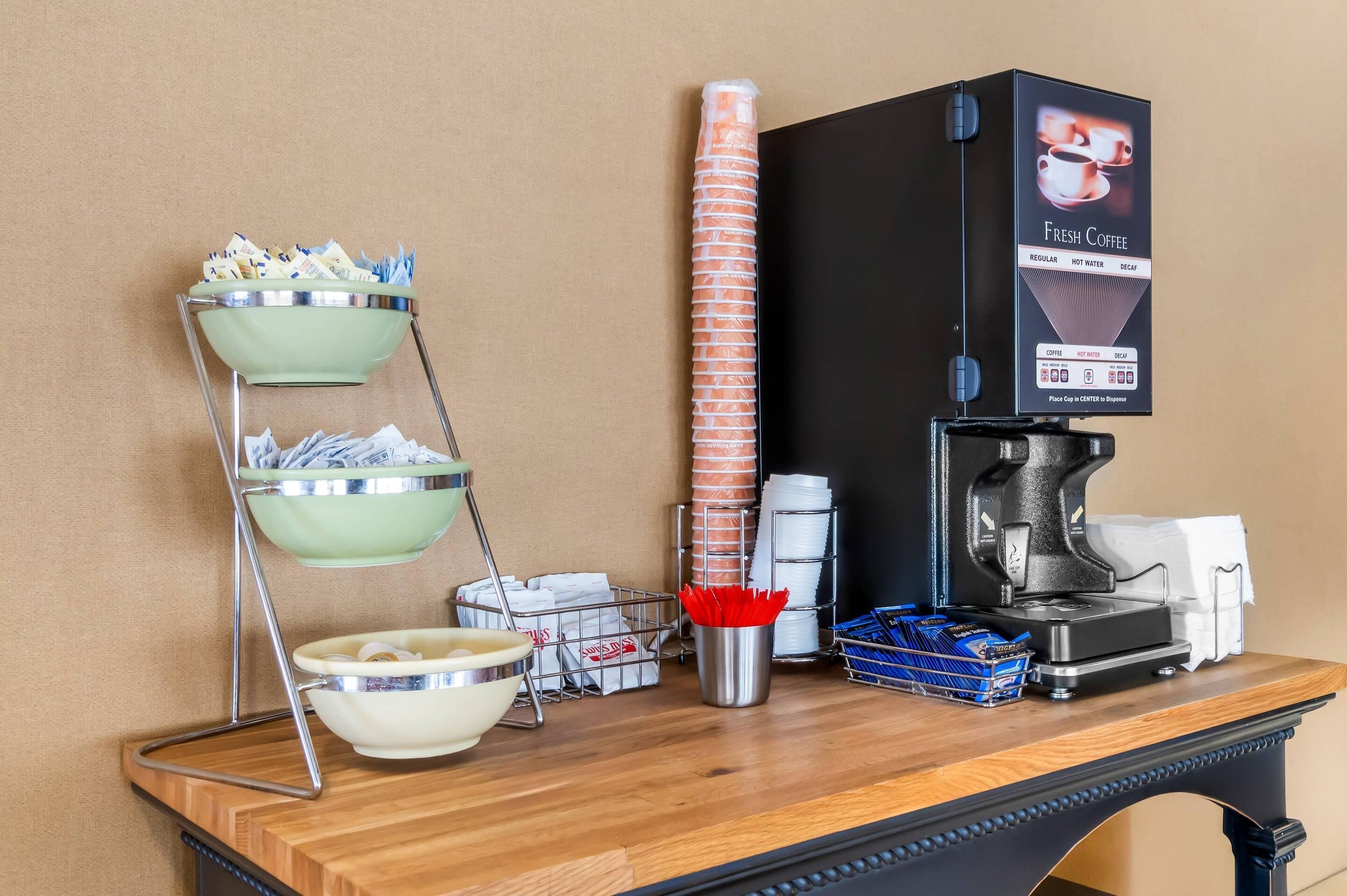 Een koffiehoek met een koffieapparaat, een koffieautomaat en een drielaags plateau met bekers en servetten.