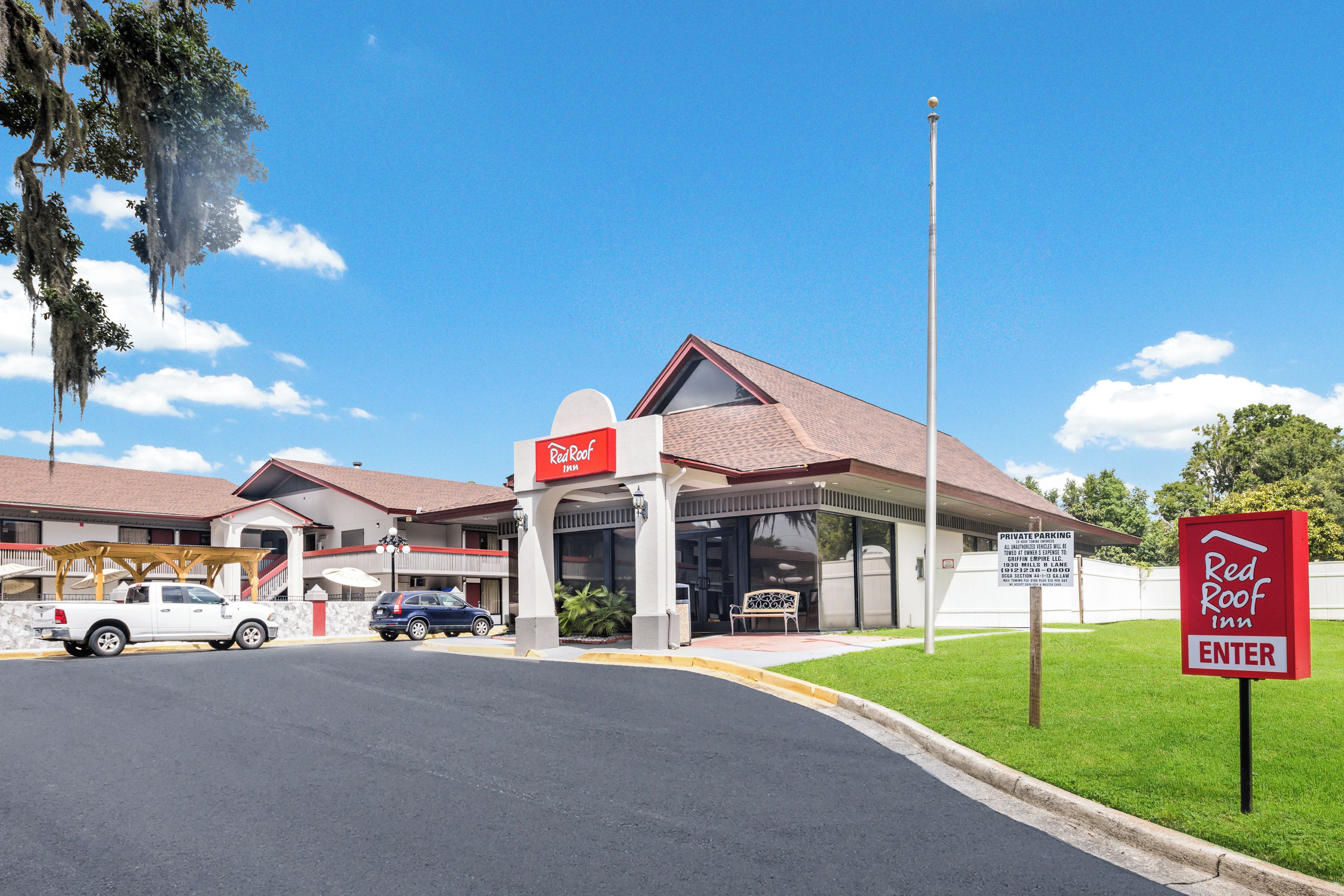 Un Red Roof Inn con zona de estacionamiento techada, un letrero que indica estacionamiento privado y un cielo azul despejado.