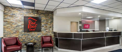 A reception area with a Red Roof Inn sign, a reception desk, two leather chairs, and a small table.